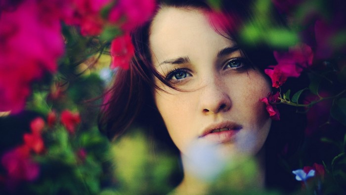 Close-up portrait of a young woman with blue eyes and freckles surrounded by flowers