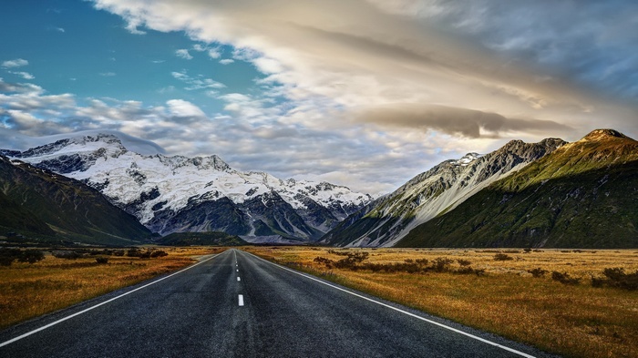 Road leading to snow-capped mountains under cloudy sky