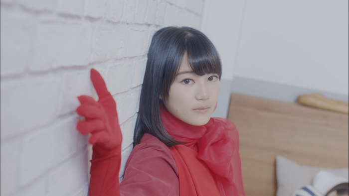 Woman in red dress and gloves leaning against a white brick wall