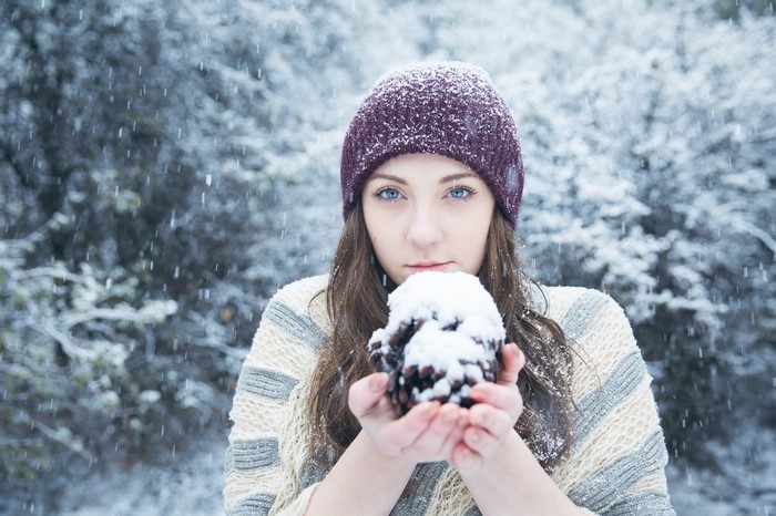 Woman in a purple hat holding a snow-covered pinecone