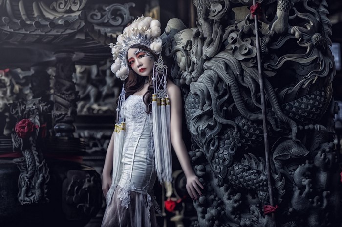 Woman in elaborate headdress and white dress with dragon sculpture