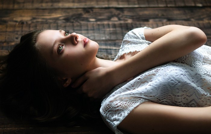 Woman lying on wooden floor wearing white lace top