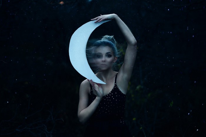 Woman holding a crescent moon in a dark forest