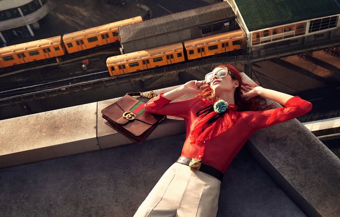 Woman in red blouse and glasses on rooftop with Gucci bag