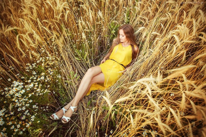 Woman in yellow dress lying in a wheat field