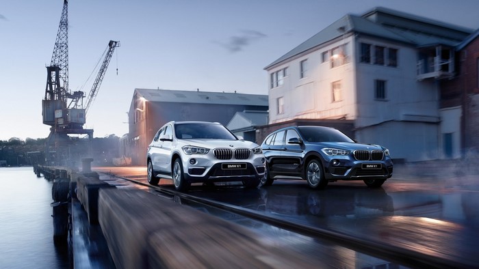 Two BMW X1 SUVs at a Harbor with Cranes