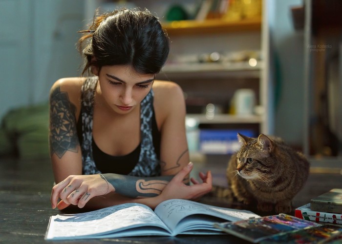 Woman with tattoos reading a book with a cat