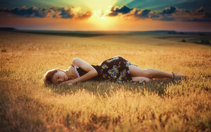 Woman sleeping in a field at sunset