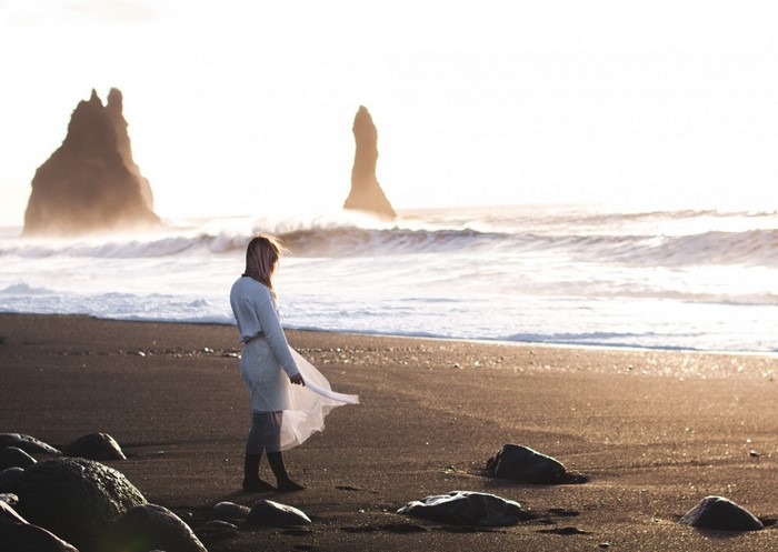 Woman in white dress on black sand beach with rock formations