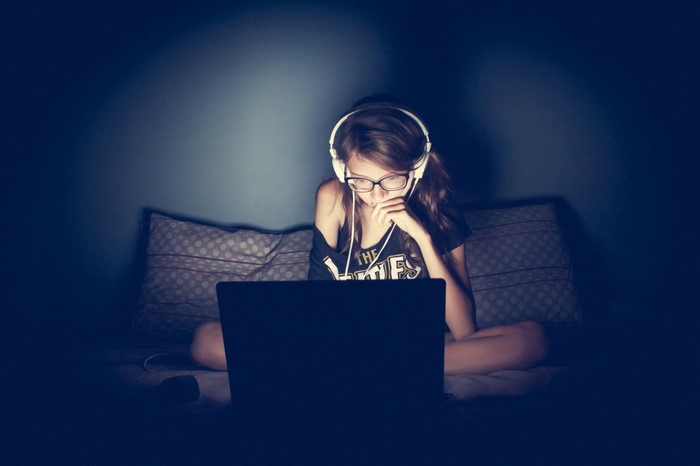 Girl with headphones and glasses using a laptop in the dark