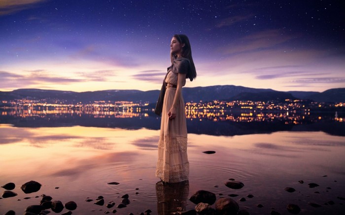 Woman standing in water at night with city lights reflection