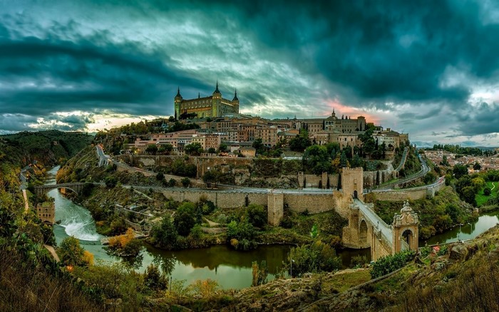 Toledo cityscape with Alcázar and river bridge at sunset