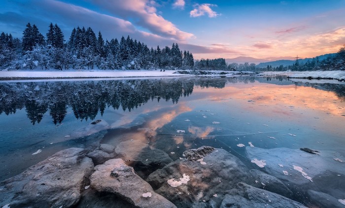 Snowy forest reflected in a frozen river at sunset