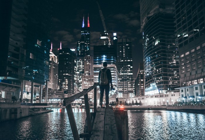 Man with backpack and camera on wooden platform overlooking Chicago skyline at night