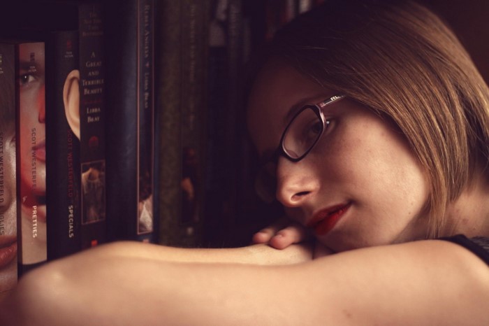 Woman with glasses resting head on arms in front of bookshelf