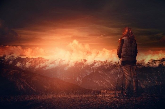 Woman with hiking poles overlooking mountains at sunset
