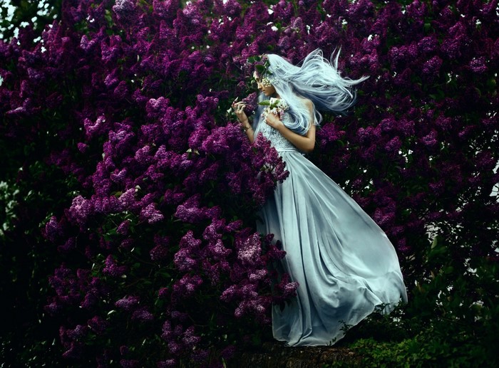 Woman with light blue hair in a light blue dress among purple lilacs
