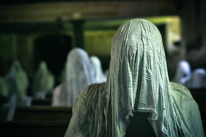 Ghosts covered in white sheets sitting in pews