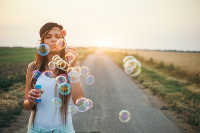 Woman blowing bubbles on a road at sunset