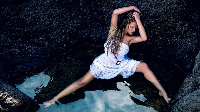 Woman in white dress posing in water among rocks