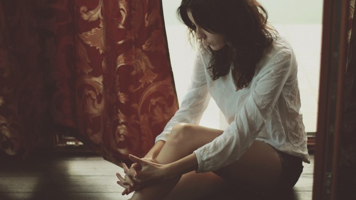 Woman sitting indoors with patterned curtains