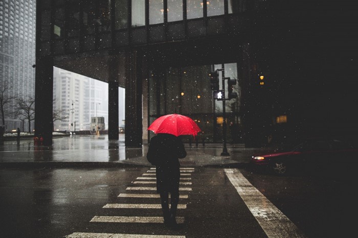 Person with red umbrella crossing street in rain at night