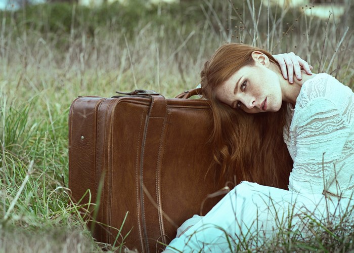 Woman with red hair resting on a suitcase in a field