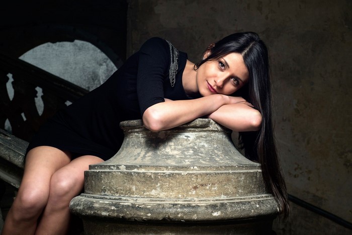 Woman in black dress sitting on stone pillar
