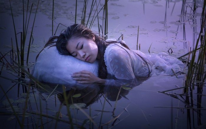 Woman sleeping on a pillow in water with reeds