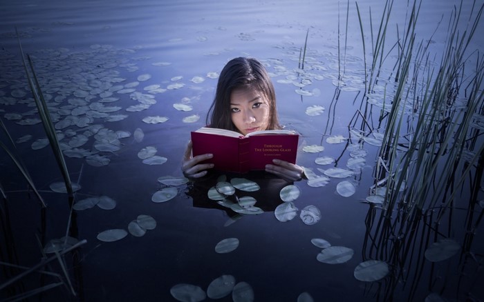 Woman reading a book in water with lily pads