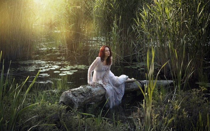 Woman in white dress sitting on a log in a swamp