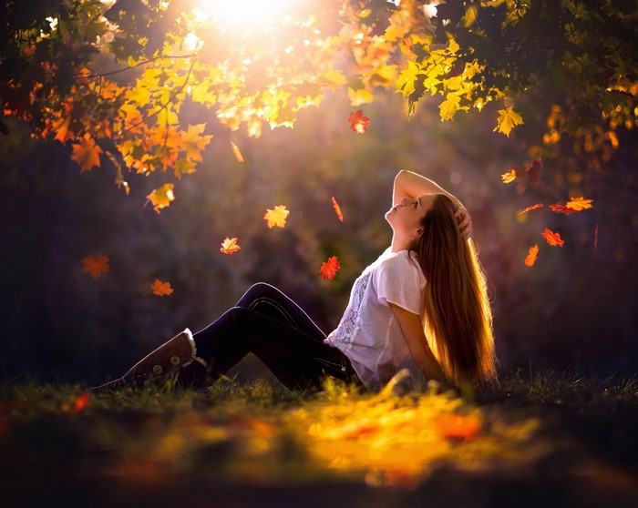 Woman sitting in autumn leaves during sunset