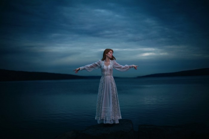 Woman in a white dress by the water at dusk