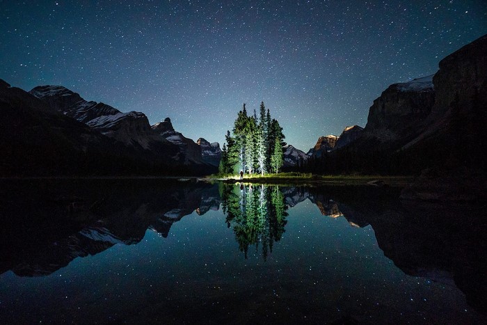 Island of trees reflected in a lake under a starry sky