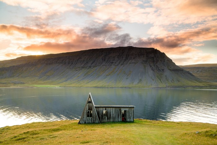 Wooden cabin by a lake with a mountain at sunset