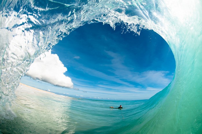 Surfer inside a wave tube with blue sky and clouds