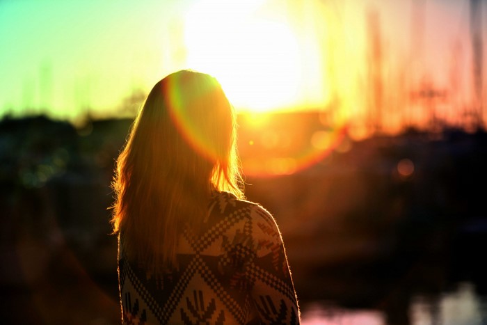 Woman in sweater watching sunset with lens flare