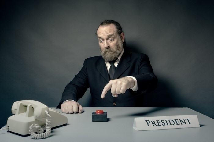 Man in suit points to red button on desk