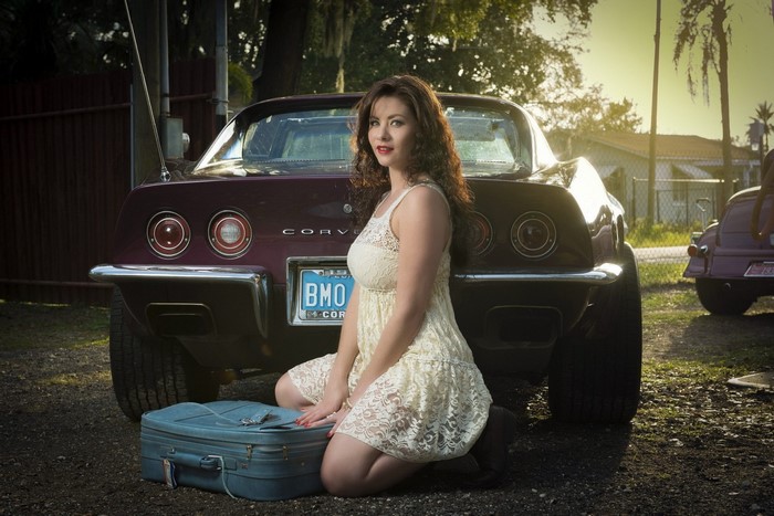 Woman in lace dress posing with a vintage Corvette