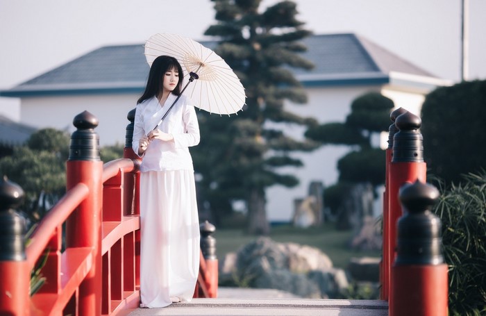Asian woman in white holding an umbrella on a red bridge