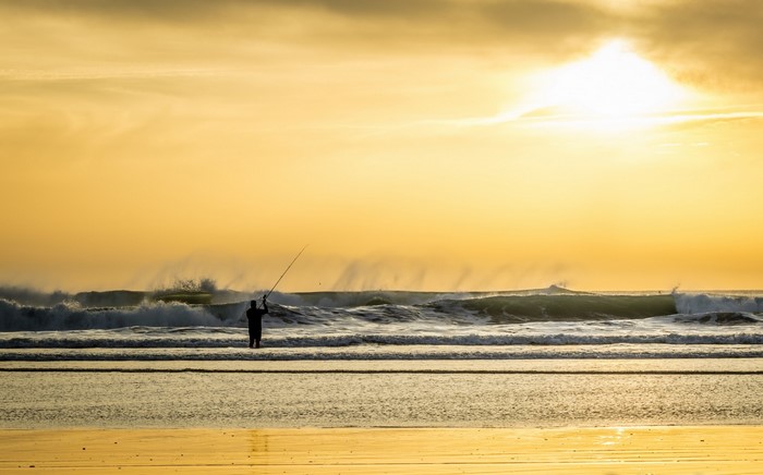 Fisherman casting line into ocean waves at sunset