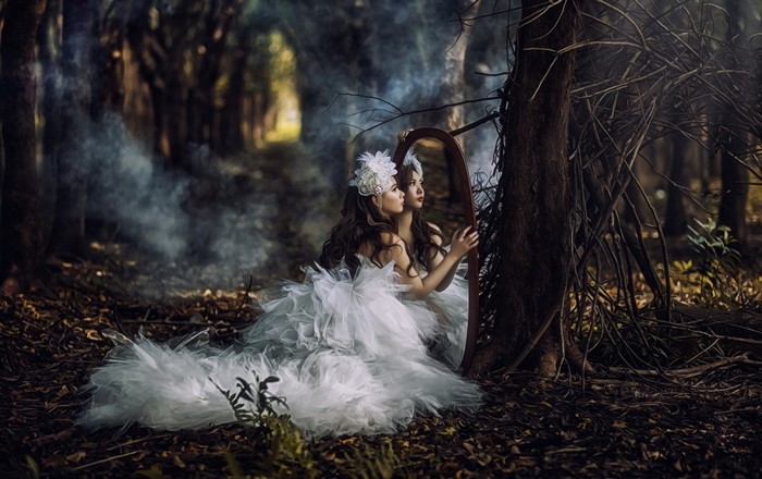 Woman in white dress looking in a mirror in a dark forest