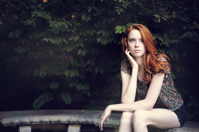 Redhead woman sitting on a stone bench in front of foliage