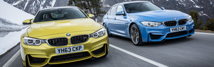 Two BMW M3 sedans driving on a mountain road
