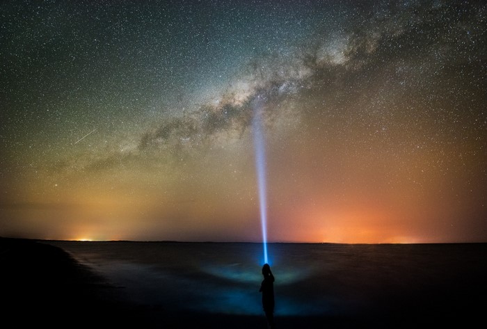Person shining flashlight at the Milky Way over the ocean