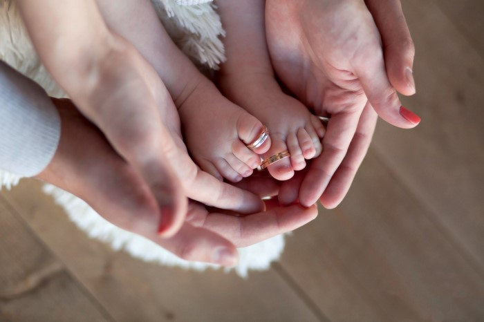 Adult hands holding baby feet with rings