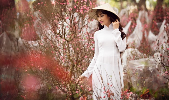 Woman in white dress and conical hat among peach blossoms