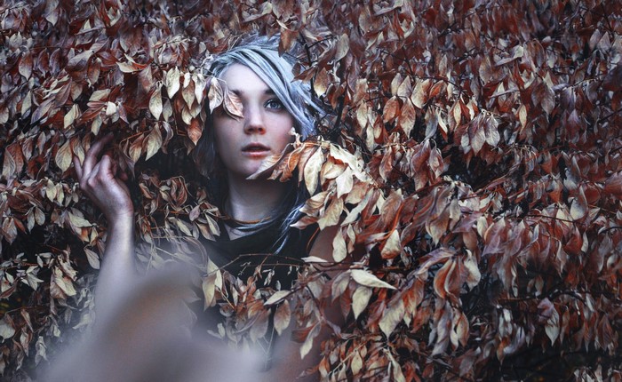 Woman with grey hair peeking through autumn leaves