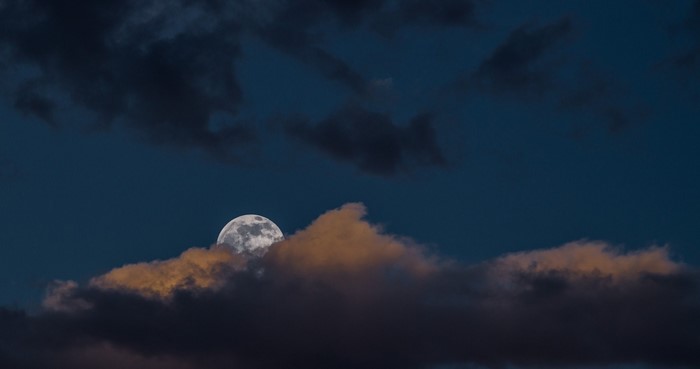 Moon peeking through clouds at dusk