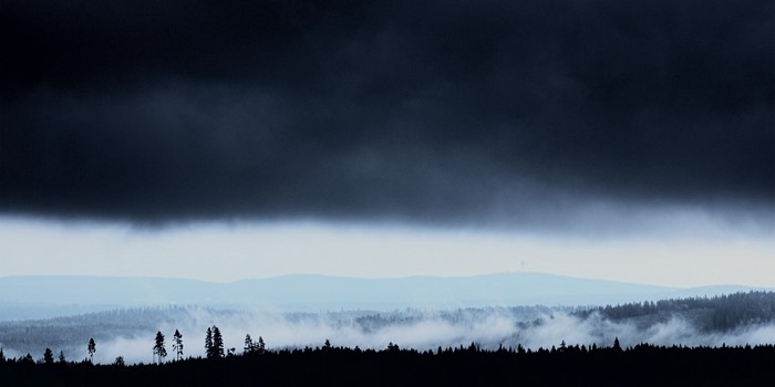 Dark storm clouds over misty forest and mountains